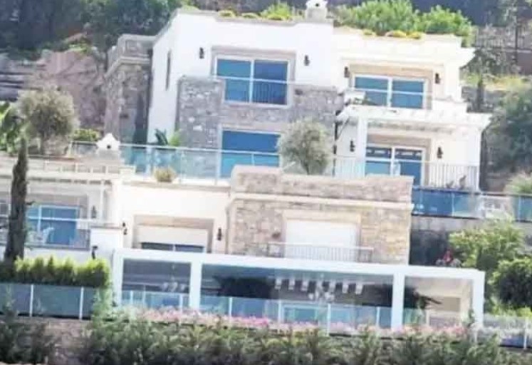 Bodrum-Çamlıköy’de tepede konumlanmış, birden fazla balkonu ve terası bulunan modern, çok katlı lüks bir villa; gün batımında deniz manzarasına karşı görüntülenmiş.